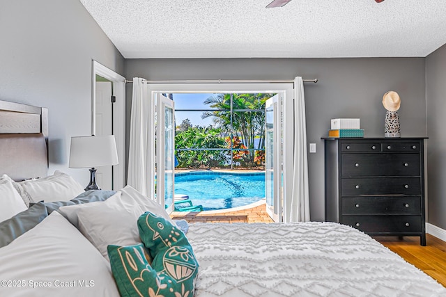 bedroom featuring access to outside, wood finished floors, baseboards, and a textured ceiling