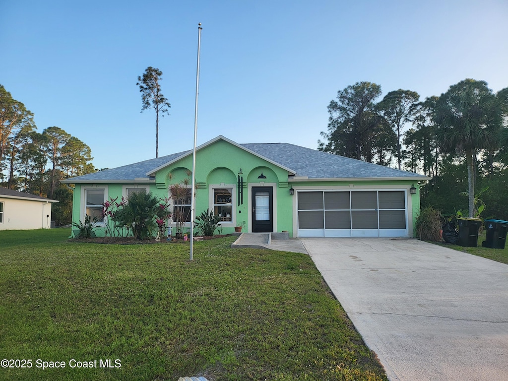 ranch-style home featuring concrete driveway, roof with shingles, an attached garage, a front yard, and stucco siding