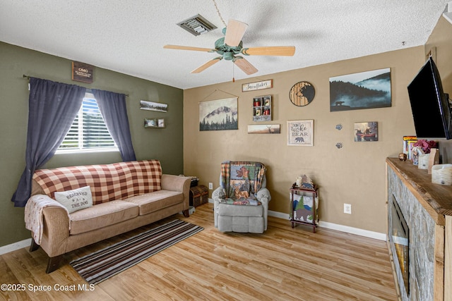 living area featuring ceiling fan, a textured ceiling, visible vents, and wood finished floors