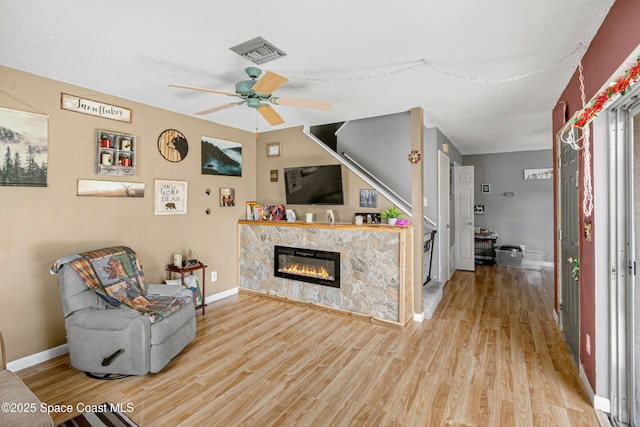 living area with a fireplace, wood finished floors, visible vents, and baseboards