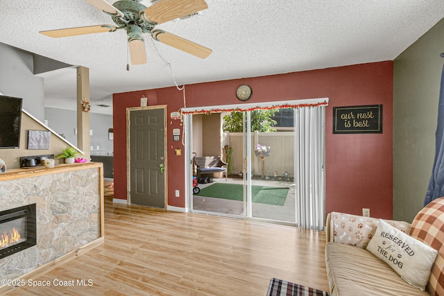 living area featuring baseboards, ceiling fan, wood finished floors, a textured ceiling, and a fireplace