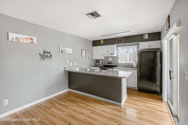 kitchen with a peninsula, a sink, visible vents, light wood-style floors, and freestanding refrigerator