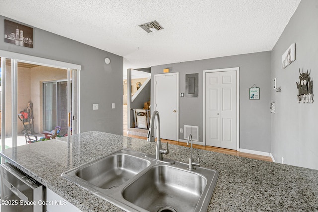 kitchen featuring a textured ceiling, stainless steel dishwasher, a sink, and visible vents