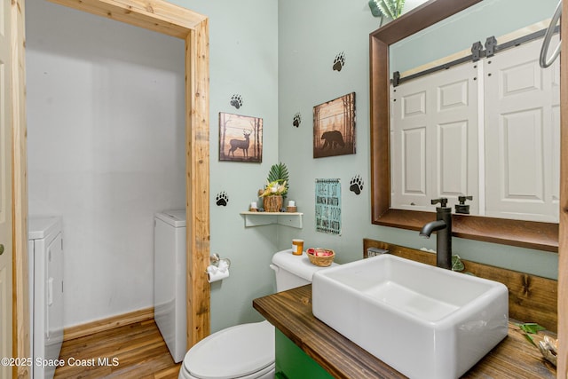 half bath featuring wood finished floors, washing machine and clothes dryer, a sink, and toilet