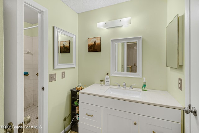 bathroom featuring a textured ceiling, tiled shower, and vanity