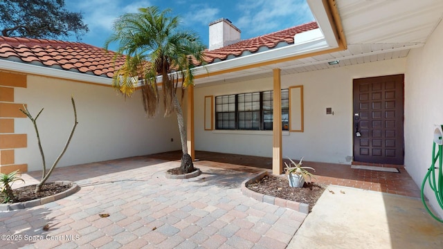 entrance to property with a tiled roof, a patio area, and stucco siding