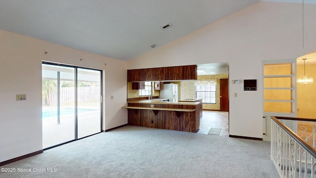 kitchen featuring high vaulted ceiling, a notable chandelier, light colored carpet, a peninsula, and freestanding refrigerator