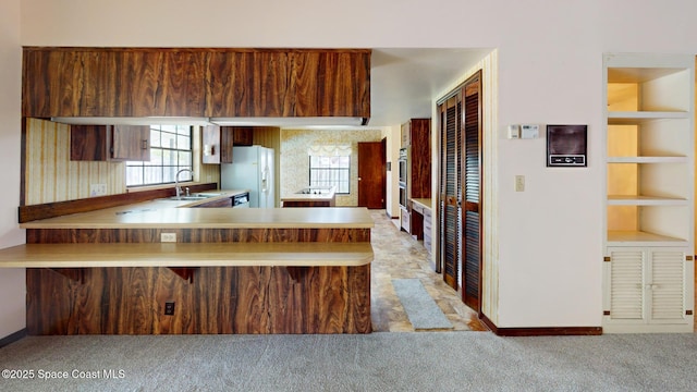 kitchen with light countertops, light carpet, a sink, white fridge with ice dispenser, and a peninsula