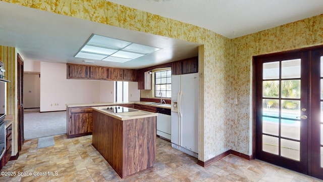 kitchen featuring light countertops, a sink, white appliances, a peninsula, and wallpapered walls