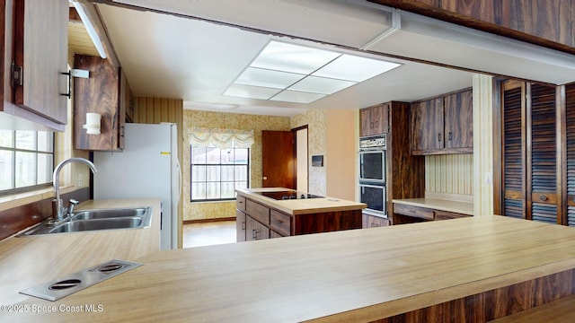 kitchen with double oven, a sink, butcher block countertops, black electric cooktop, and wallpapered walls