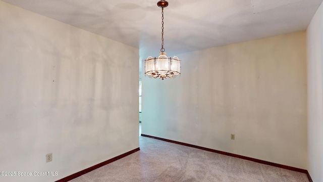 carpeted empty room featuring baseboards and an inviting chandelier