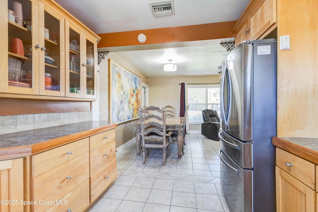 kitchen featuring light tile patterned floors, visible vents, glass insert cabinets, freestanding refrigerator, and baseboards