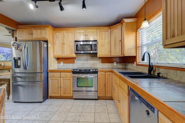 kitchen featuring light tile patterned floors, stainless steel appliances, a sink, backsplash, and decorative light fixtures