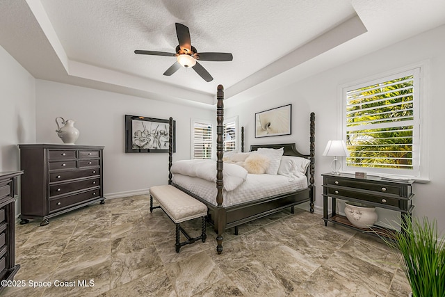 bedroom featuring baseboards, a textured ceiling, a raised ceiling, and a ceiling fan