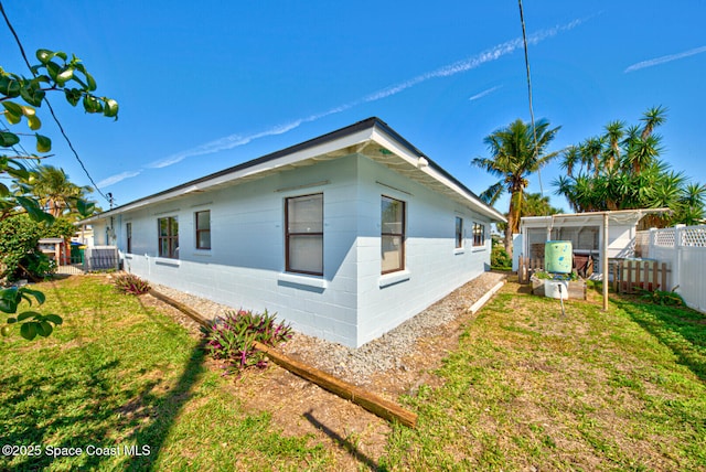 view of side of property featuring a lawn, concrete block siding, and fence