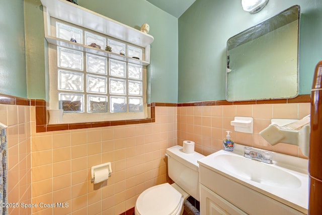 bathroom featuring toilet, wainscoting, tile walls, and vanity