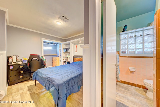 bedroom featuring ornamental molding, visible vents, tile walls, and wood finished floors