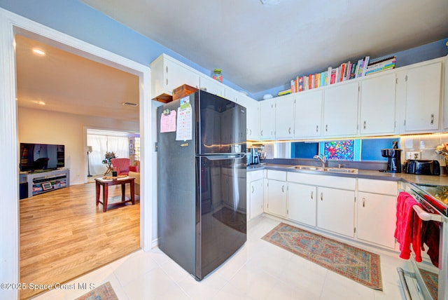 kitchen with light tile patterned floors, white cabinets, freestanding refrigerator, stainless steel electric stove, and a sink