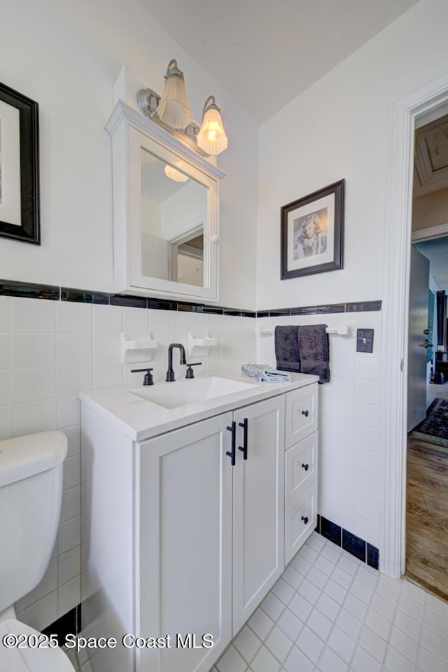 bathroom with a wainscoted wall, tile walls, toilet, vanity, and tile patterned flooring