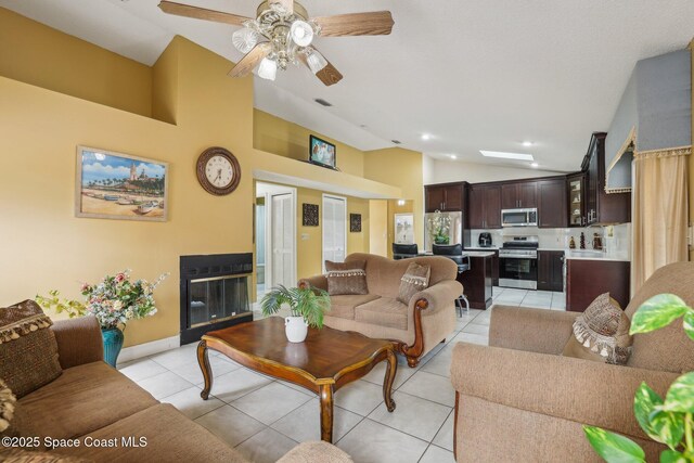 living room with visible vents, a glass covered fireplace, light tile patterned flooring, vaulted ceiling, and ceiling fan