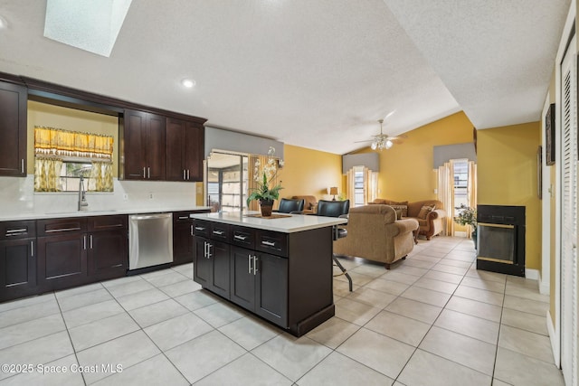 kitchen featuring light tile patterned floors, vaulted ceiling with skylight, dishwasher, light countertops, and a sink