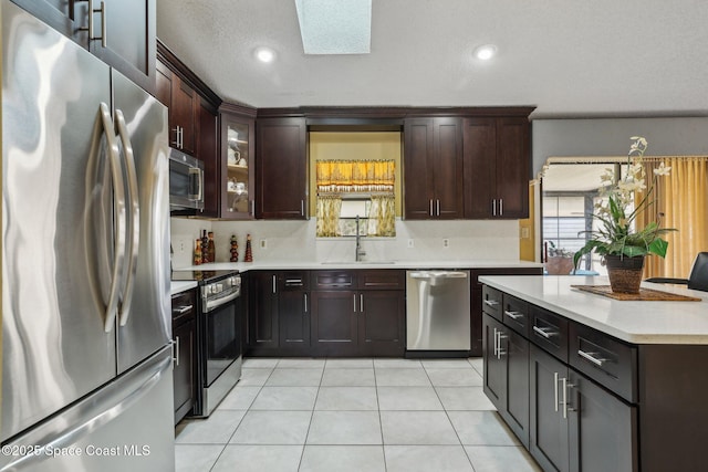 kitchen featuring light tile patterned flooring, a skylight, a sink, light countertops, and appliances with stainless steel finishes