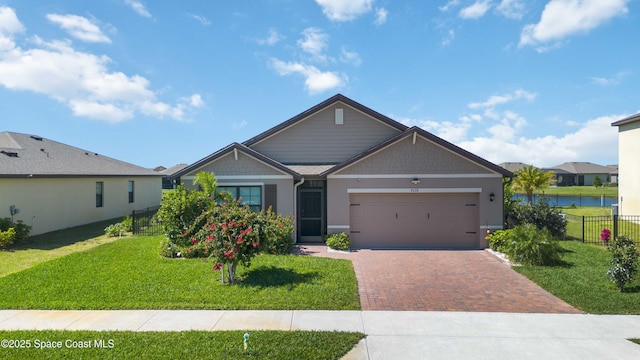 craftsman-style house featuring an attached garage, a water view, fence, decorative driveway, and a front lawn