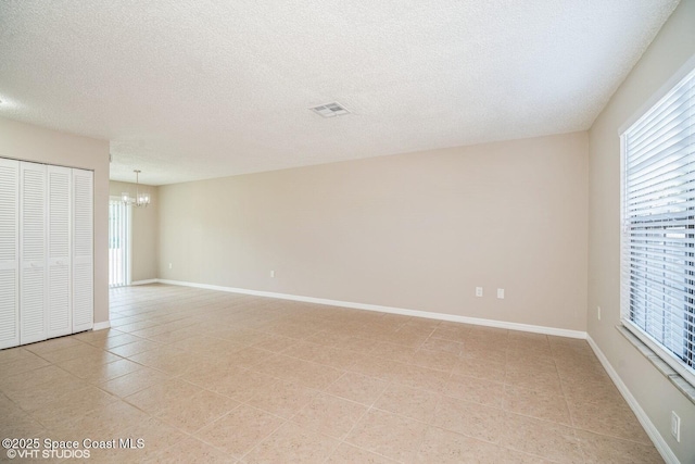 empty room featuring baseboards, a textured ceiling, light tile patterned flooring, and an inviting chandelier