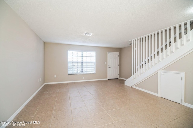 interior space featuring light tile patterned floors, a textured ceiling, visible vents, baseboards, and stairway