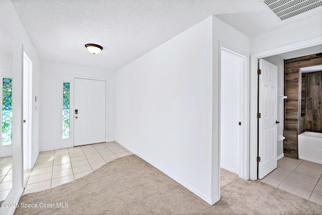 entryway with light colored carpet, visible vents, a textured ceiling, and light tile patterned floors