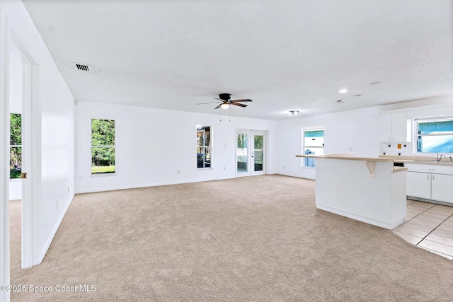 unfurnished living room featuring light colored carpet, visible vents, a sink, a textured ceiling, and ceiling fan