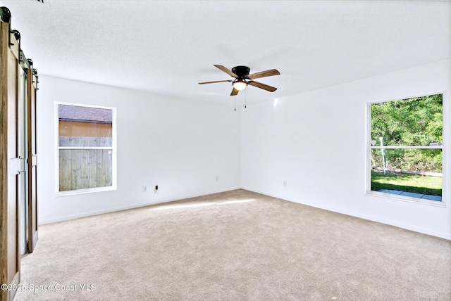 carpeted spare room featuring a ceiling fan, a textured ceiling, and a barn door