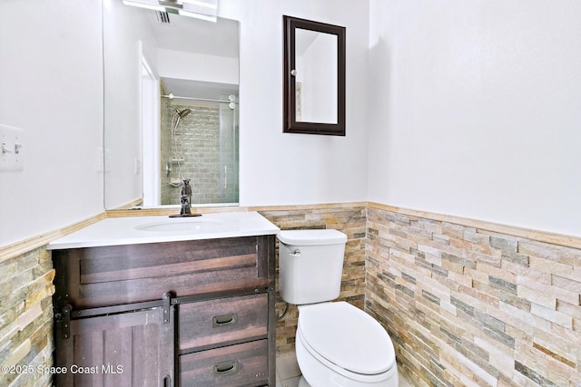 full bath with toilet, a wainscoted wall, vanity, tile walls, and a tile shower