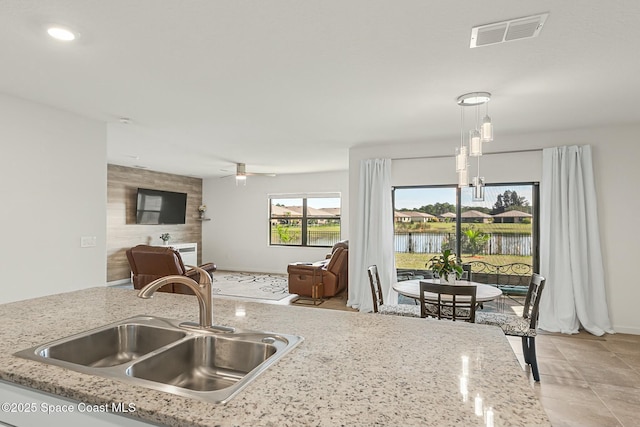 kitchen with a sink, visible vents, a ceiling fan, open floor plan, and hanging light fixtures