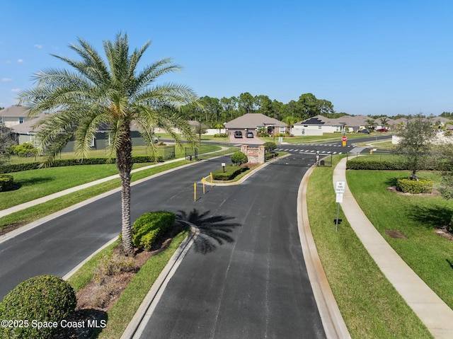 view of street featuring a gated entry, sidewalks, curbs, a residential view, and traffic signs