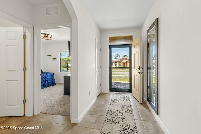 entrance foyer featuring light tile patterned floors, baseboards, visible vents, and arched walkways