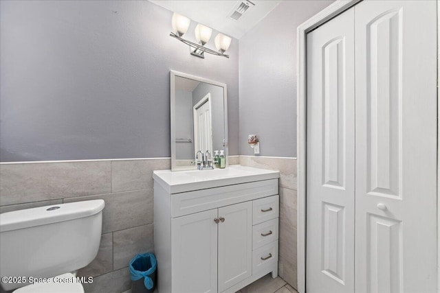 bathroom featuring toilet, vanity, visible vents, and tile walls