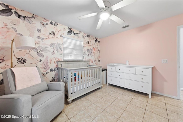 bedroom with a crib, light tile patterned floors, visible vents, baseboards, and ceiling fan