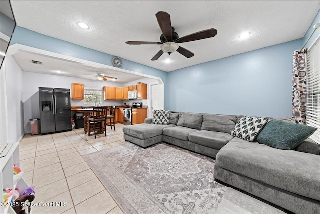 living room with light tile patterned floors, ceiling fan, visible vents, and a textured ceiling