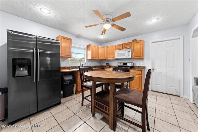 kitchen featuring stainless steel electric stove, dark countertops, white microwave, light tile patterned flooring, and refrigerator with ice dispenser