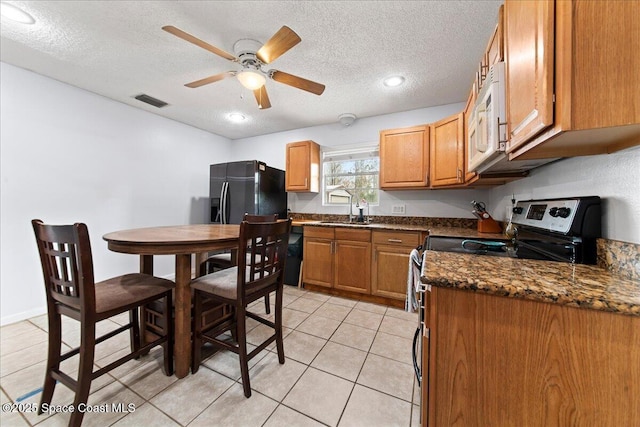 kitchen with stainless steel electric stove, black fridge with ice dispenser, white microwave, a sink, and a textured ceiling