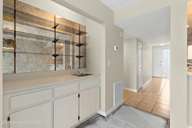 bar featuring visible vents, a sink, a textured ceiling, wet bar, and baseboards