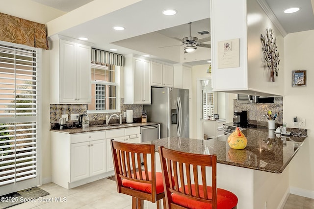 kitchen with a ceiling fan, a peninsula, a sink, stainless steel appliances, and a kitchen breakfast bar