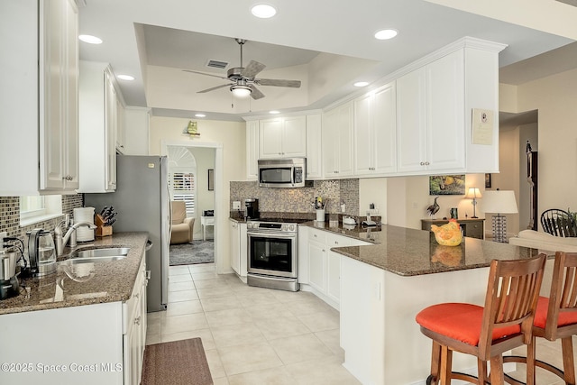 kitchen with visible vents, a tray ceiling, a peninsula, stainless steel appliances, and white cabinetry