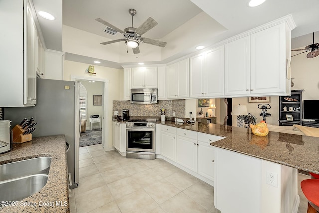 kitchen featuring stainless steel appliances, a peninsula, white cabinets, a raised ceiling, and ceiling fan