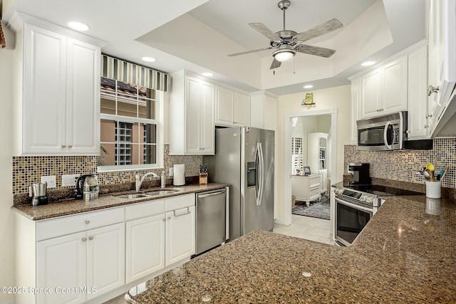 kitchen with a sink, a tray ceiling, tasteful backsplash, appliances with stainless steel finishes, and white cabinets