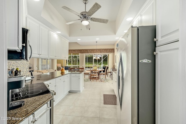 kitchen with light tile patterned floors, a peninsula, a tray ceiling, white cabinets, and appliances with stainless steel finishes