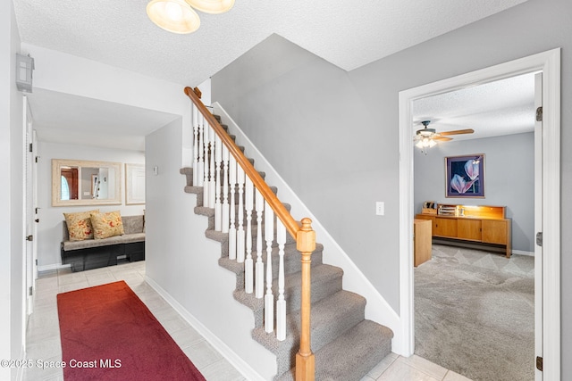 stairway featuring carpet, a ceiling fan, a textured ceiling, baseboards, and tile patterned floors