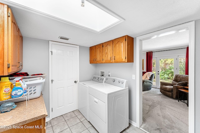 clothes washing area featuring light tile patterned floors, a skylight, visible vents, cabinet space, and washing machine and clothes dryer