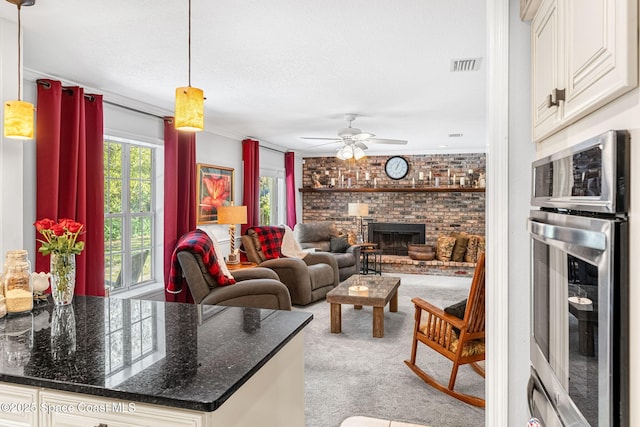 living area featuring visible vents, a ceiling fan, light colored carpet, brick wall, and a brick fireplace